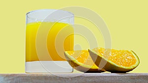 Orange juice in a glass with orange slices on a wooden tray on a bright yellow background. Natural fresh juice. Summer drink