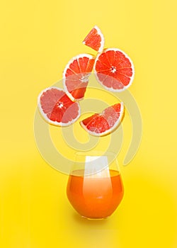 Orange juice in a glass with slices of orange on yellow background.