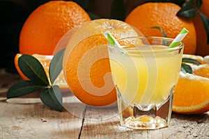 Orange juice in a glass with striped straws and large ripe oranges, selective focus