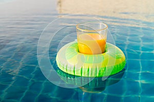 Orange juice glass with swim ring at outdoor swimming pool