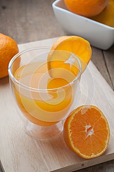 Orange juice glass on a wooden cutting board and wooden floors.