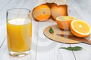 Orange juice in a glass on a wooden table, fresh cut oranges in the background