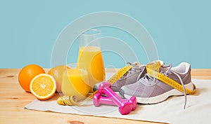Orange juice, oranges, sneakers, dumbbells and measuring tape on blue background