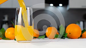 Orange juice pouring into glass on white table. Citrus juice splash