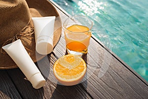 Orange juice, straw hat, sunblock and sunglasses by poolside