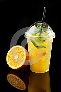 orange juice in takeaway plastic cup with fresh fruits on dark background