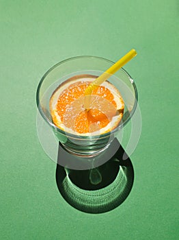 Orange juice with yellow straw in a glas concept on green background. Tropical summer minimal concept sunlit with sharp shadows