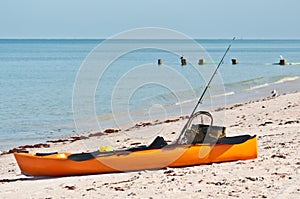 Orange kayak, fitted for fishing, resting on sandy, tropical beach