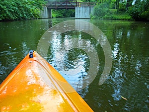 Orange kayak on an idyllic river scene with green foliage.