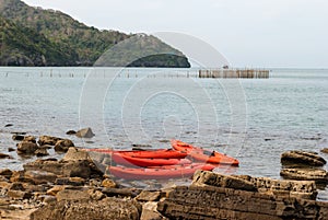 Orange kayaks left on rock beach with the sea background