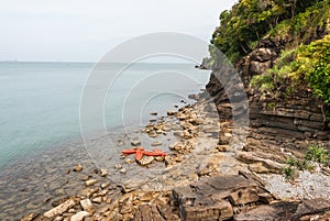 Orange kayaks left on rock beach with the sea background