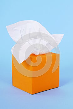 Orange kleenex style tissue box, white soft tissues, blue background, copy space