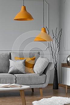 Orange lamp above grey scandinavian sofa in modern interior