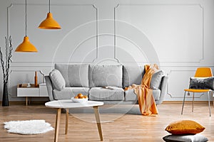 Orange lamp above grey scandinavian sofa