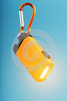 Orange led Flashlight with a carabiner on a blue background. LED lights in flight