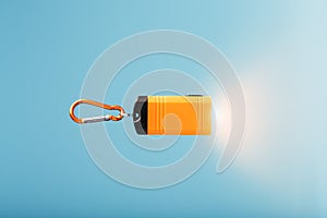 Orange led Flashlight with a carabiner on a blue background. LED lights in flight