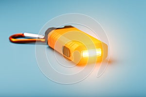 Orange led Flashlight with a carabiner on a blue background. LED lights in flight