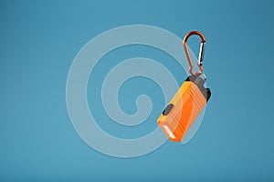 Orange led Flashlight with a carabiner on a blue background. LED lights in flight