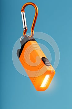 Orange led Flashlight with a carabiner on a blue background. LED lights in flight