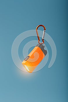 Orange led Flashlight with a carabiner on a blue background. LED lights in flight