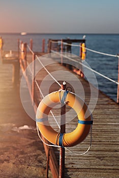 Orange life buoy hanging on an old pier by the sea