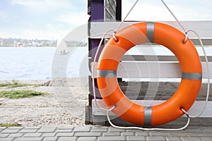 Orange life buoy hanging on white wooden fence at beach, space for text