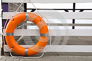 Orange life buoy hanging on white wooden fence at beach, space for text