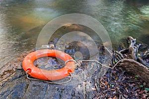 Orange life buoy over the clear water of natural stream.