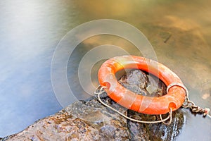 Orange life buoy over the clear water of natural stream.