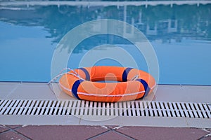 An orange life buoy rests on the edge of a blue water pool