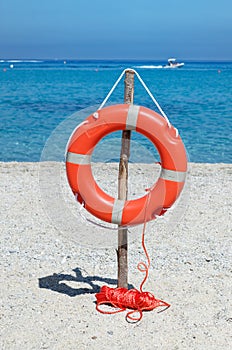 Orange life buoy on the sandy beach against blue sea water