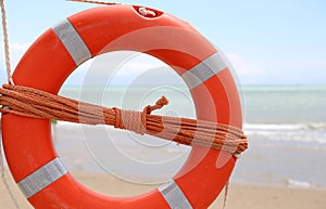 Orange life-buoy by the sea with the rescue rope