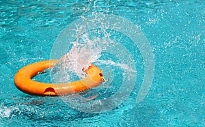 Orange life buoy is splashing with clear blue water in swimming