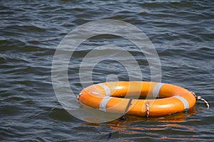 Orange life buoy on water surface as symbol of help and hope, selective focus