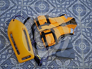 An orange life jacket, gray small rubber flippers, and an orange plastic rescue torpedo buoy for the lifeguard on the