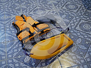 An orange life jacket, gray small rubber flippers, and an orange plastic rescue torpedo buoy for the lifeguard on the