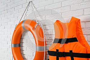 Orange life jacket and lifebuoy on white brick wall. Rescue equipment