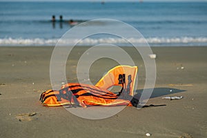 An orange life-jackets on the beach with 3 children on the background