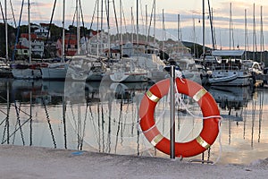 Orange life ring on the pier in the Croatian marina against the backdrop of sailing yachts. Safety on the water and saving