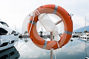 Orange lifebuoy on the background of marina. Rescue buoy hanging on metal rack for publication, poster, screensaver