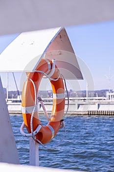 Orange lifebuoy on beach by sea. Safety equipment for rescuing people on seashore. Orange lifebuoy on the pier of blue