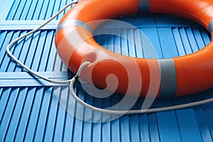 Orange lifebuoy on blue wooden background, closeup. Rescue equipment