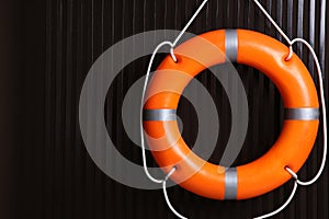 Orange lifebuoy on dark wooden background, space for text. Rescue equipment