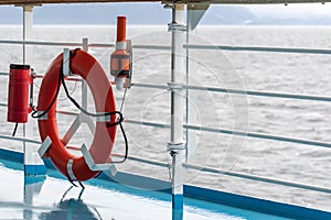 Orange lifebuoy emergency gear/ device/ equipment with reflective silver strips on cruise ship deck.
