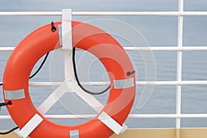 Orange lifebuoy emergency gear/ device/ equipment with reflective silver strips on cruise ship deck.