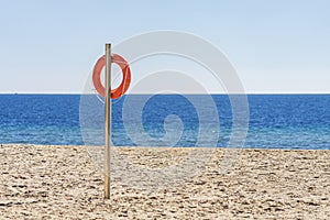 Orange lifebuoy in empty sandy beach in front of Mediterranean sea. Life saving lifeguard buoy, lifebelt on the pole