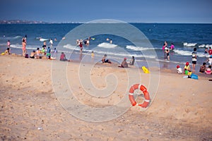 Orange lifebuoy in foreground. Blue clear sky, sea and people in