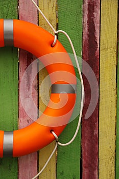 Orange lifebuoy hanging on color wooden fence. Rescue equipment