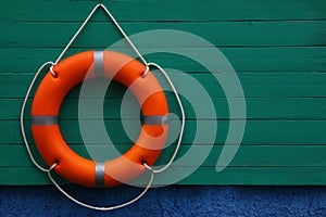 Orange lifebuoy hanging on green wooden board, space for text. Rescue equipment