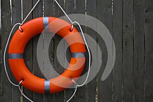 Orange lifebuoy hanging on grey wooden fence, space for text. Rescue equipment